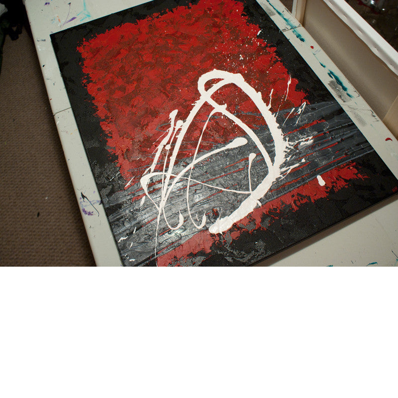 Close up image of a red, black, white and grey contemporary abstract painting on a table