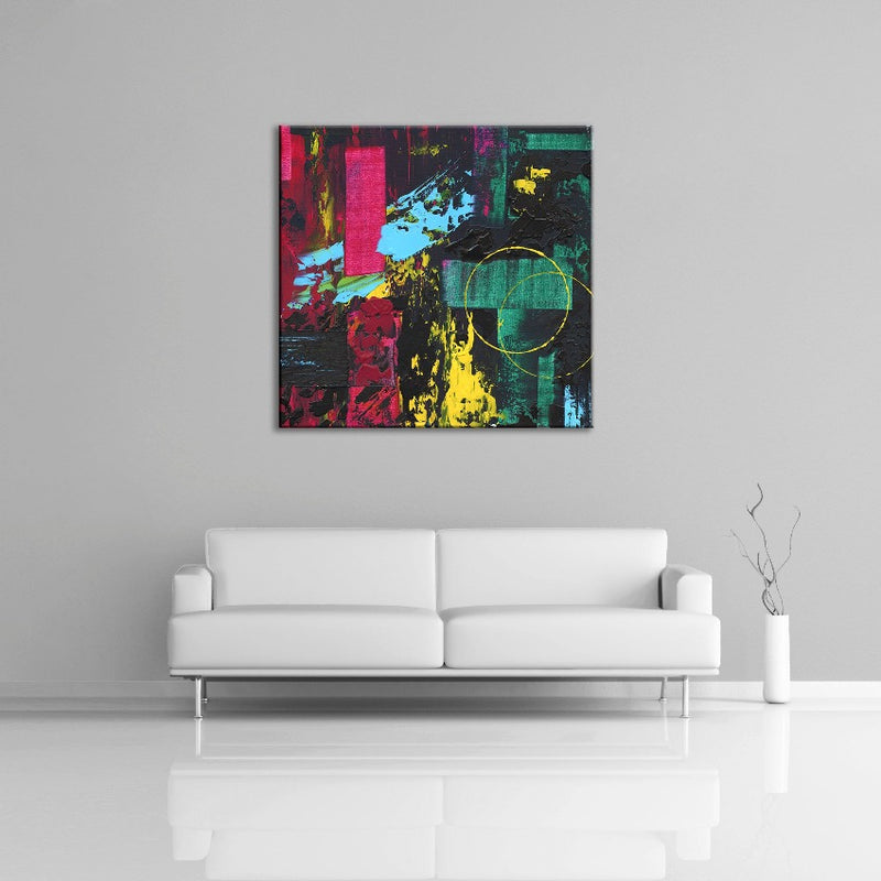 An abstract painting featuring black, green, pink, yellow and light blue paint displayed over a white couch.