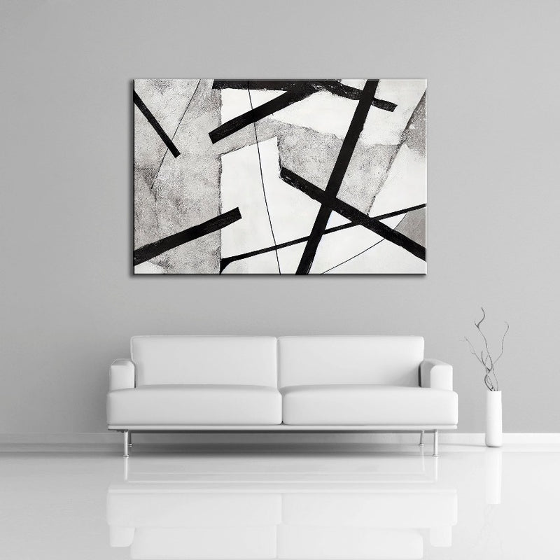 A abstract painting featuring strong black lines over the colours white and gray. Displayed over a couch.